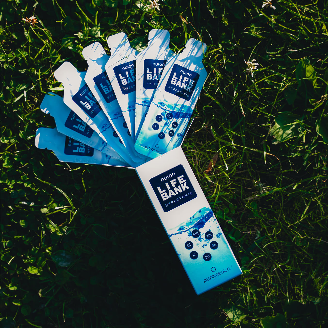 Auf dem Bild sind mehrere Verpackungen des Produkts Life Bank nuion - Hypertonisch von Puromedica zu sehen, die auf einem grünen Grasboden angeordnet sind.