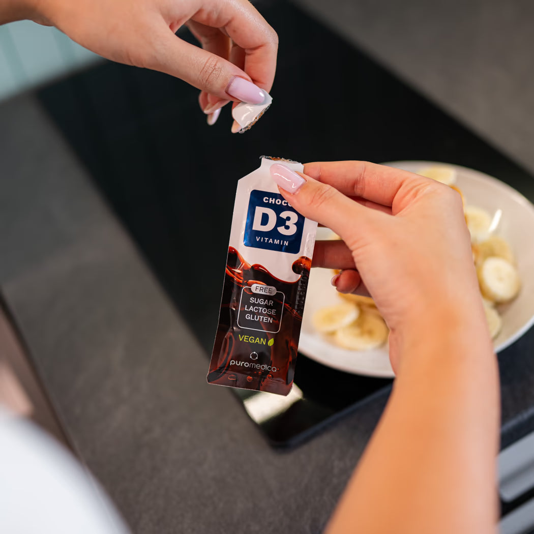 Eine Person hält ein Tütchen mit D3 Vitamin von Puromedica in der Hand und öffnet es, während sie sich in einer modernen Küche befindet.