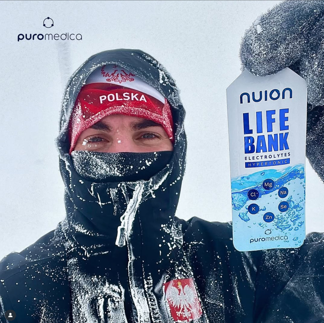Ein Mann steht in einer schneebedeckten Landschaft und hält ein Paket mit „Life Bank nuion - Hypertonisch“ in der Hand, während er in warmer, wetterfester Kleidung gekleidet ist.