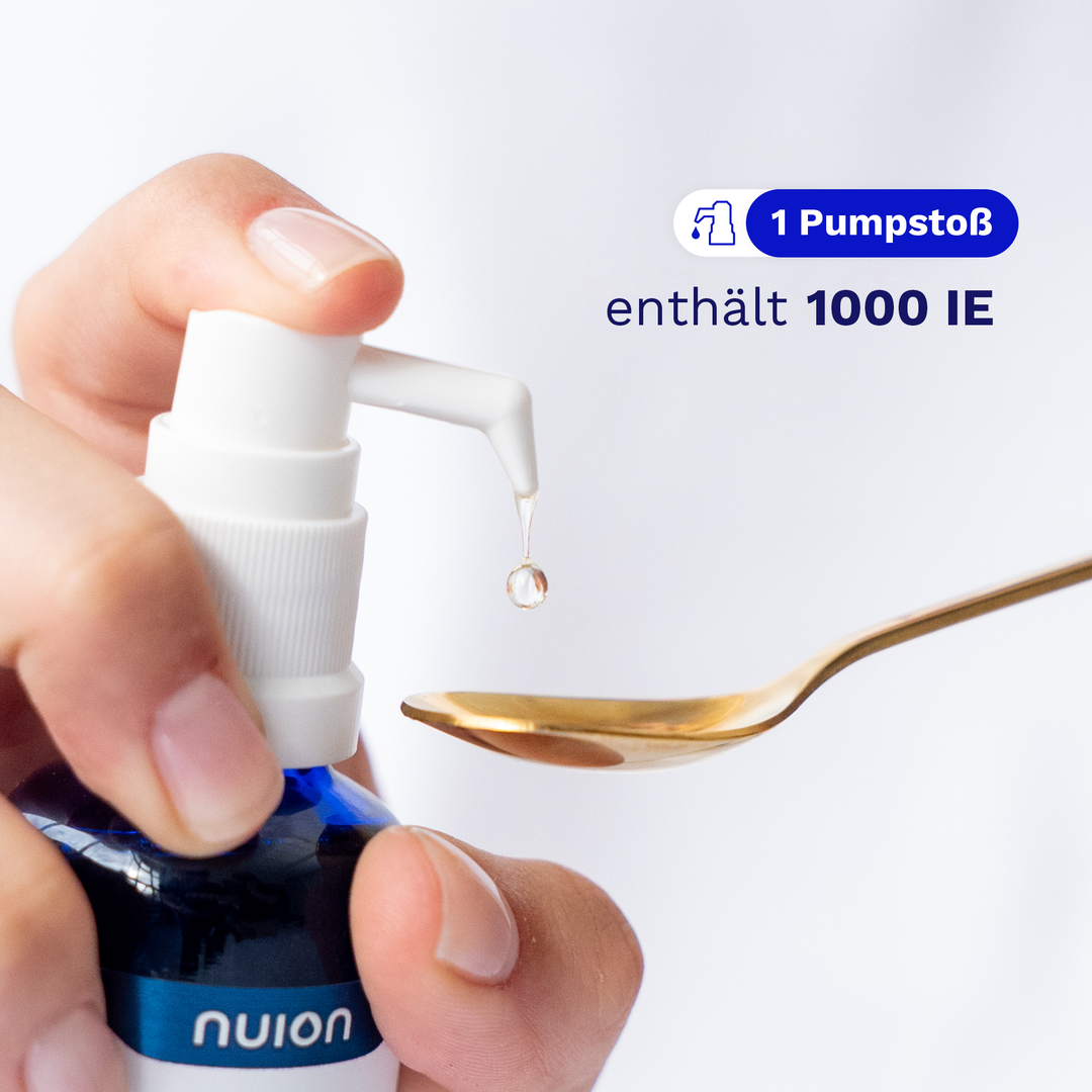 Eine Hand hält eine Flasche mit einem Pumpspender, aus dem ein Tropfen des Inhalts auf einen goldenen Löffel fällt.