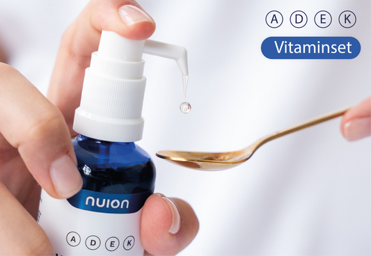 Eine Hand hält eine Flasche mit dem Vitamin ADEK von Puromedica, während die andere Hand einen kleinen Löffel hält, auf dem sich ein Tropfen des Vitamins befindet.